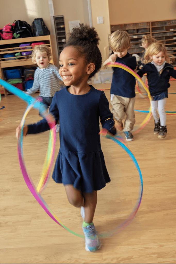 a joyful group of young school children playing with rainbow ribbon wands in a classroom or gym setting
