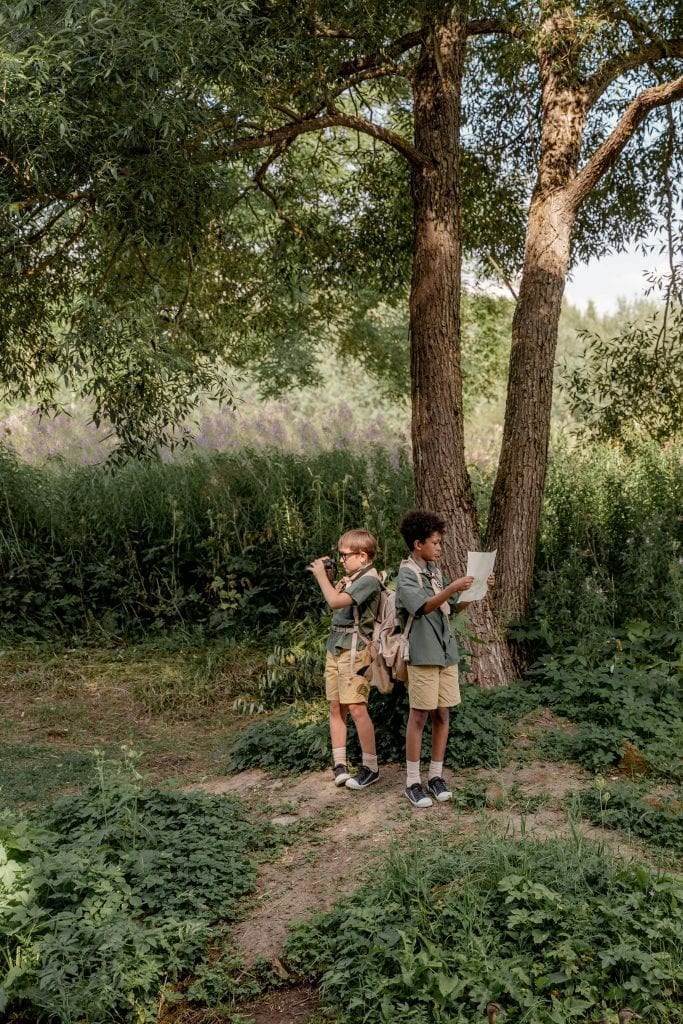 Boys Standing on Grass Field Near Brown Tree
