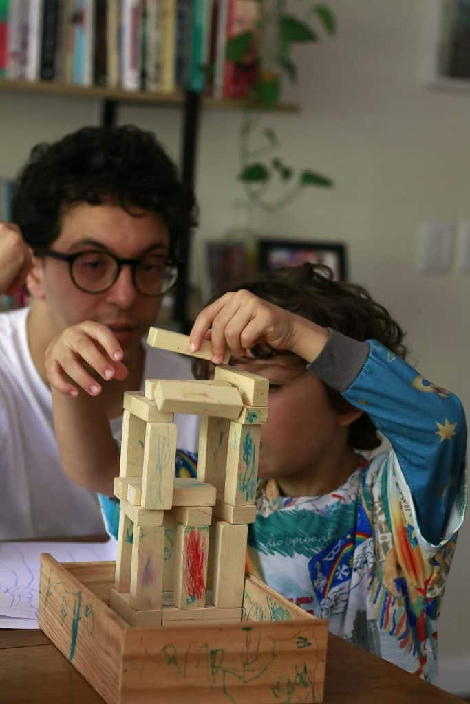 a young child and an adult engaged in a quiet, focused indoor activity—building a wooden block tower together.