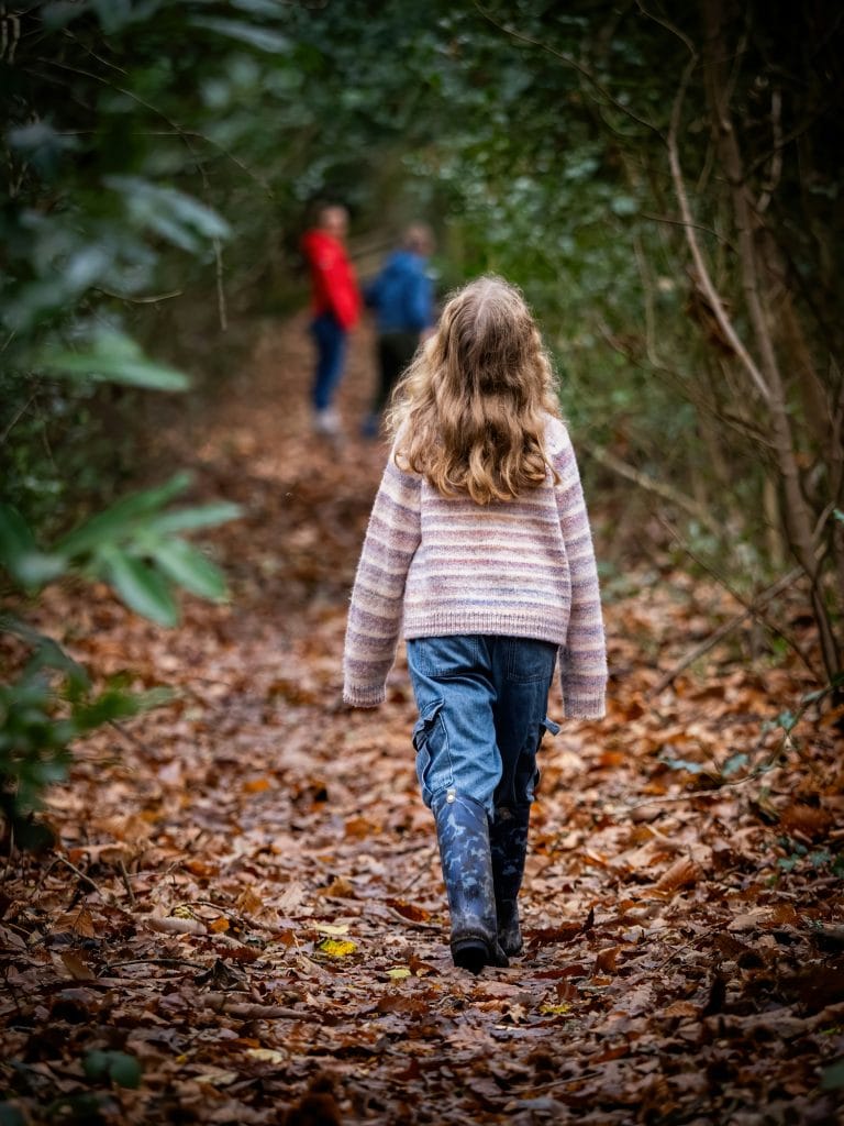 a young girl walking along a narrow forest trail in autumn, surrounded by dense green foliag