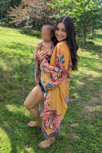 Mother standing barefoot on grass while holding her child, enjoying grounding and connecting with nature