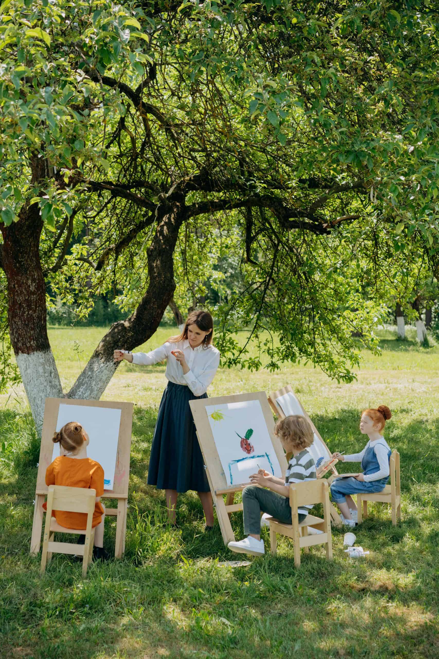 a serene outdoor art class for children taking place beneath a lush, green tree in a sunlit meadow