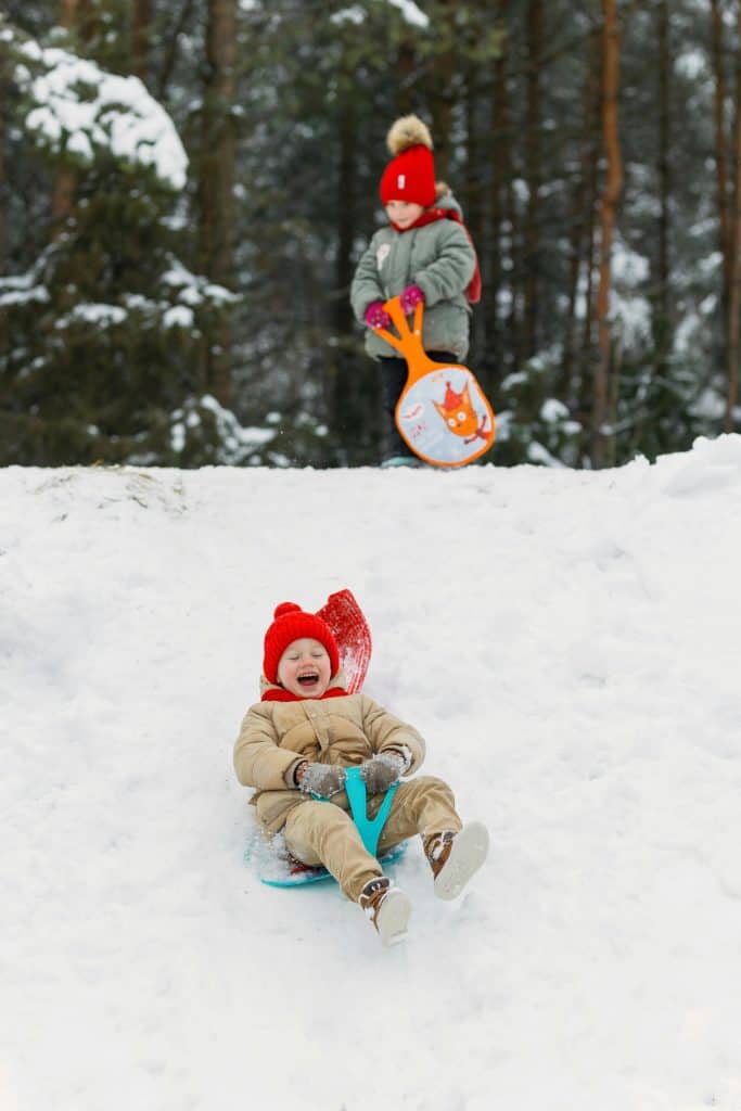 Laughing Little Boy Sliding Down a Snowy Hill on an Apple Sled