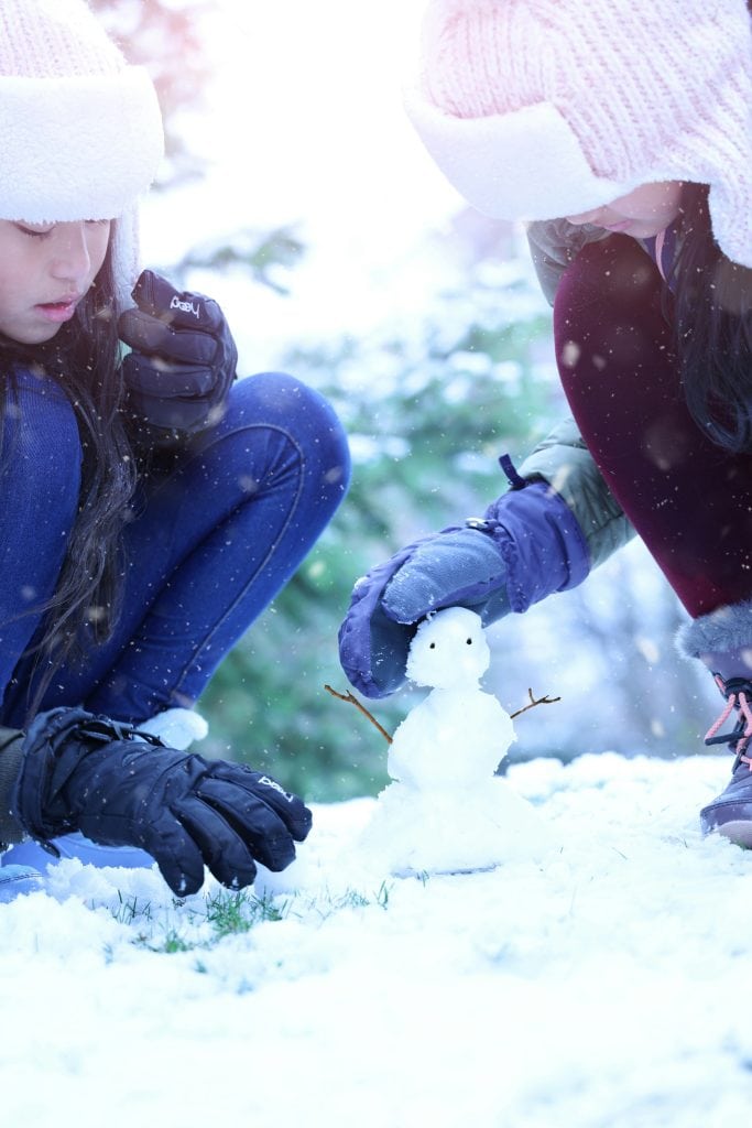 two girls building a tiny snowman on a fresh bed of snow.