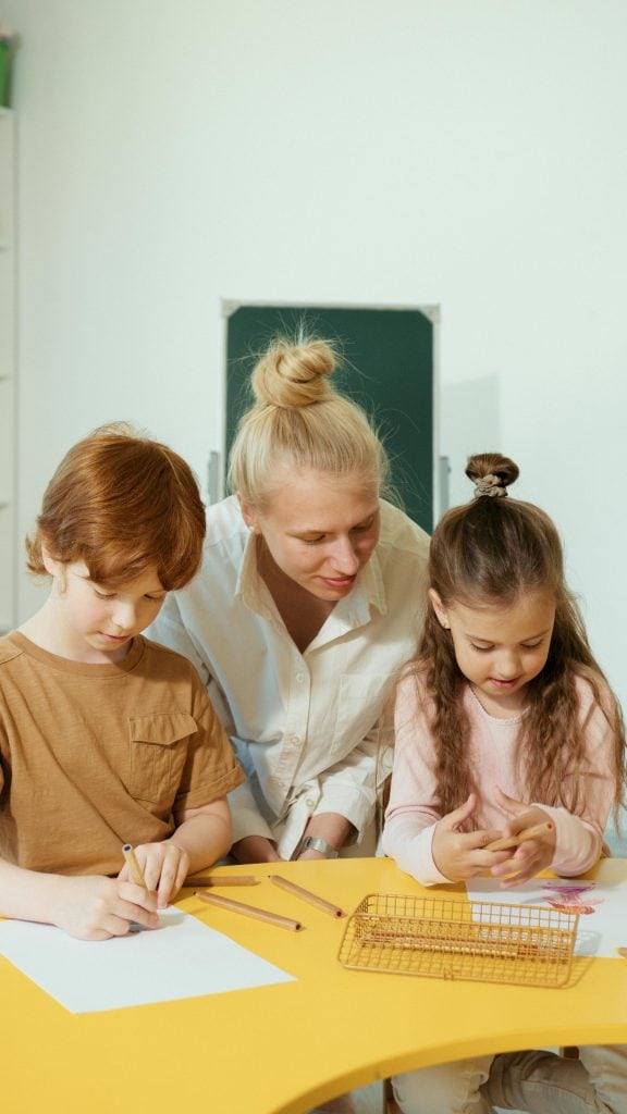 a warm and focused classroom moment between a teacher and two young children engaged in a creative activity
