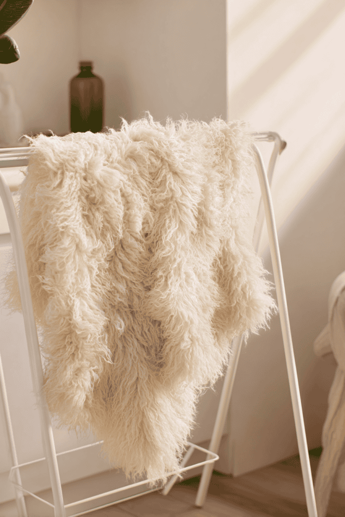 a freshly cleaned, cream-colored faux sheepskin rug draped over a minimalist white drying rack