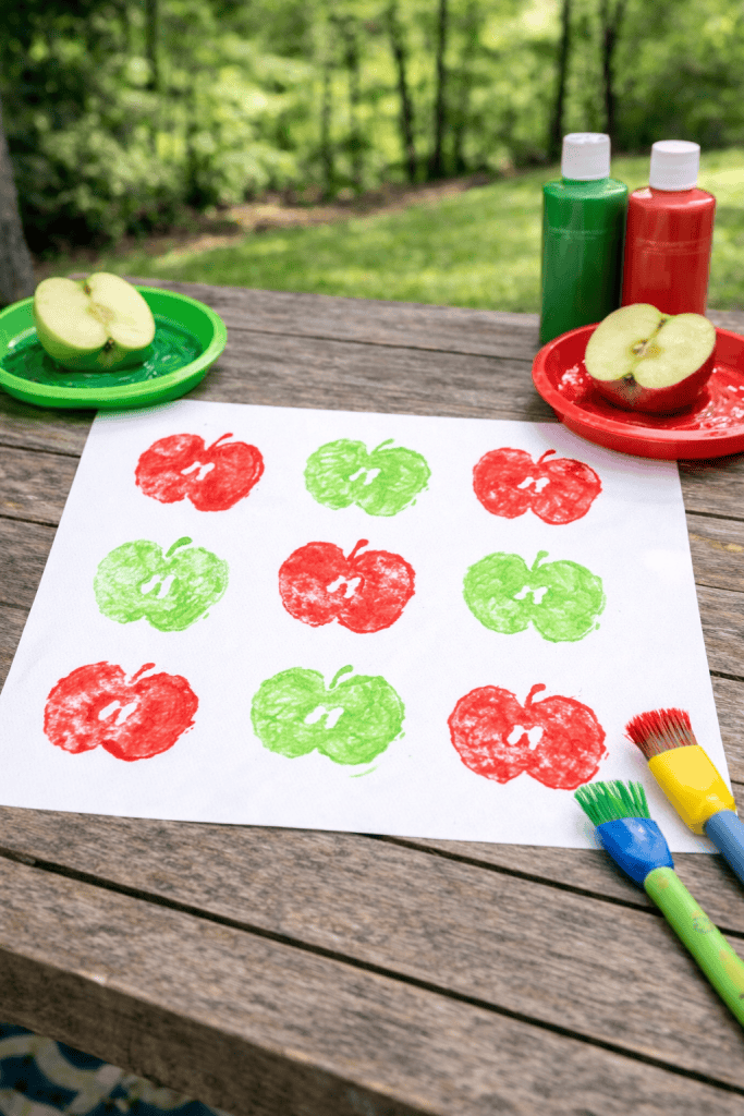 a children’s apple stamping art activity set outdoors on a rustic wooden table