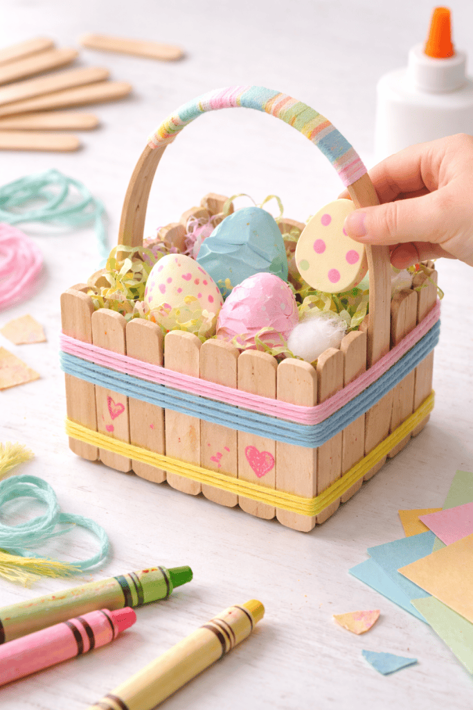 a miniature Easter basket made entirely from wooden craft sticks, displayed on a child-friendly craft table.