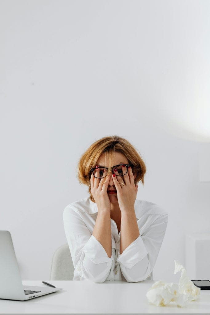 a stressed woman sitting at a minimalist white desk in a modern, bright office space