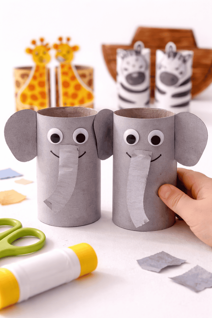 Toddler-made toilet paper roll elephant pair with googly eyes and paper ears, standing on a white surface