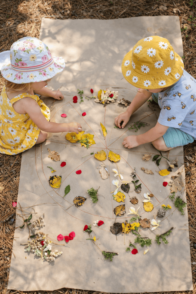 two young children engaged in a creative, nature-based outdoor activity.