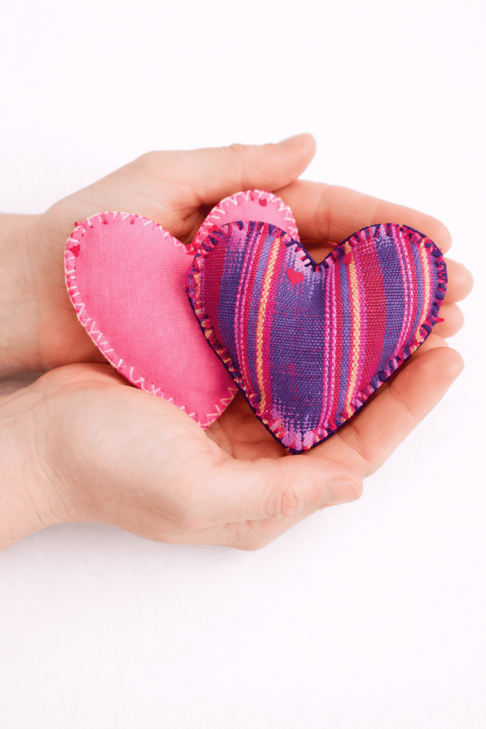 two handmade heart-shaped fabric hand warmers being gently held in a pair of cupped hands