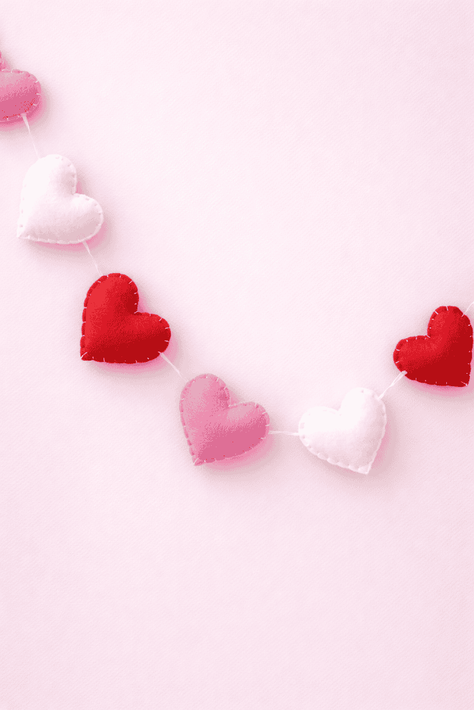 a handmade Valentine’s Day heart garland bunting against a soft pastel pink background.