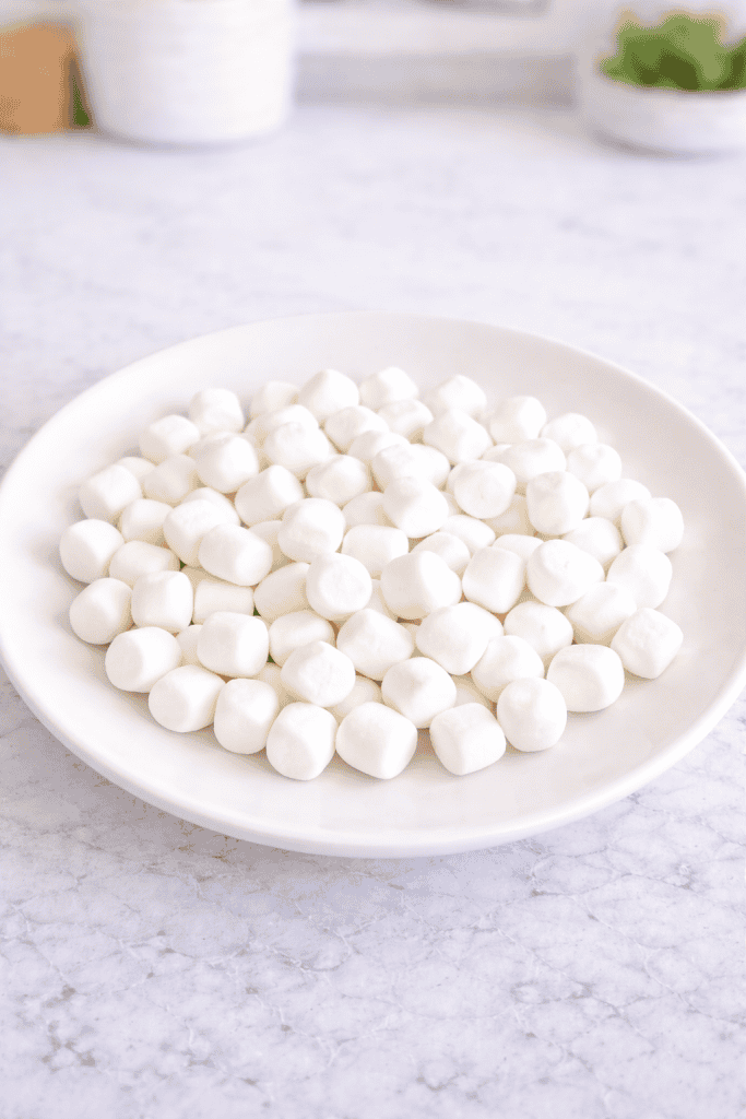 a full plate of mini marshmallows neatly piled in the center of a clean, matte white ceramic dish.