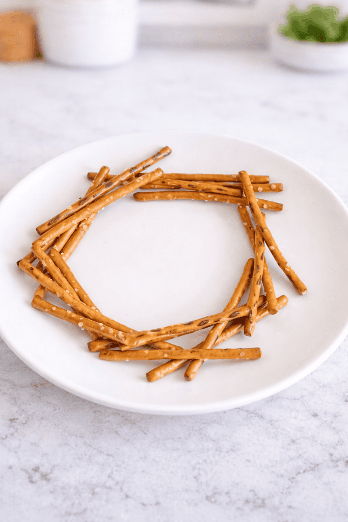 a clean, minimalistic food presentation featuring salted pretzel sticks arranged in a circular pattern on a matte white ceramic plate.