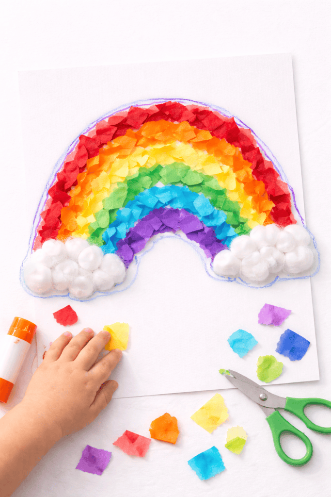 Toddler-made tissue paper rainbow collage with cotton ball clouds on white cardstock