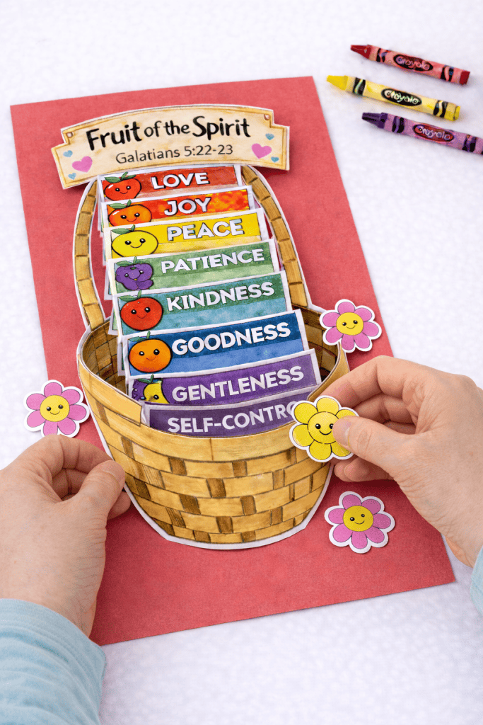 Hands decorating a 3D Fruit of the Spirit basket craft with flower cutouts