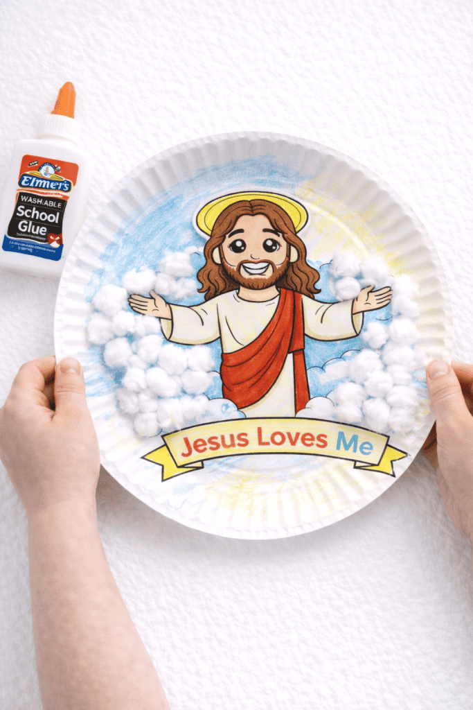 Child holding a paper plate craft with a Jesus illustration glued in the center and cotton ball clouds around it.