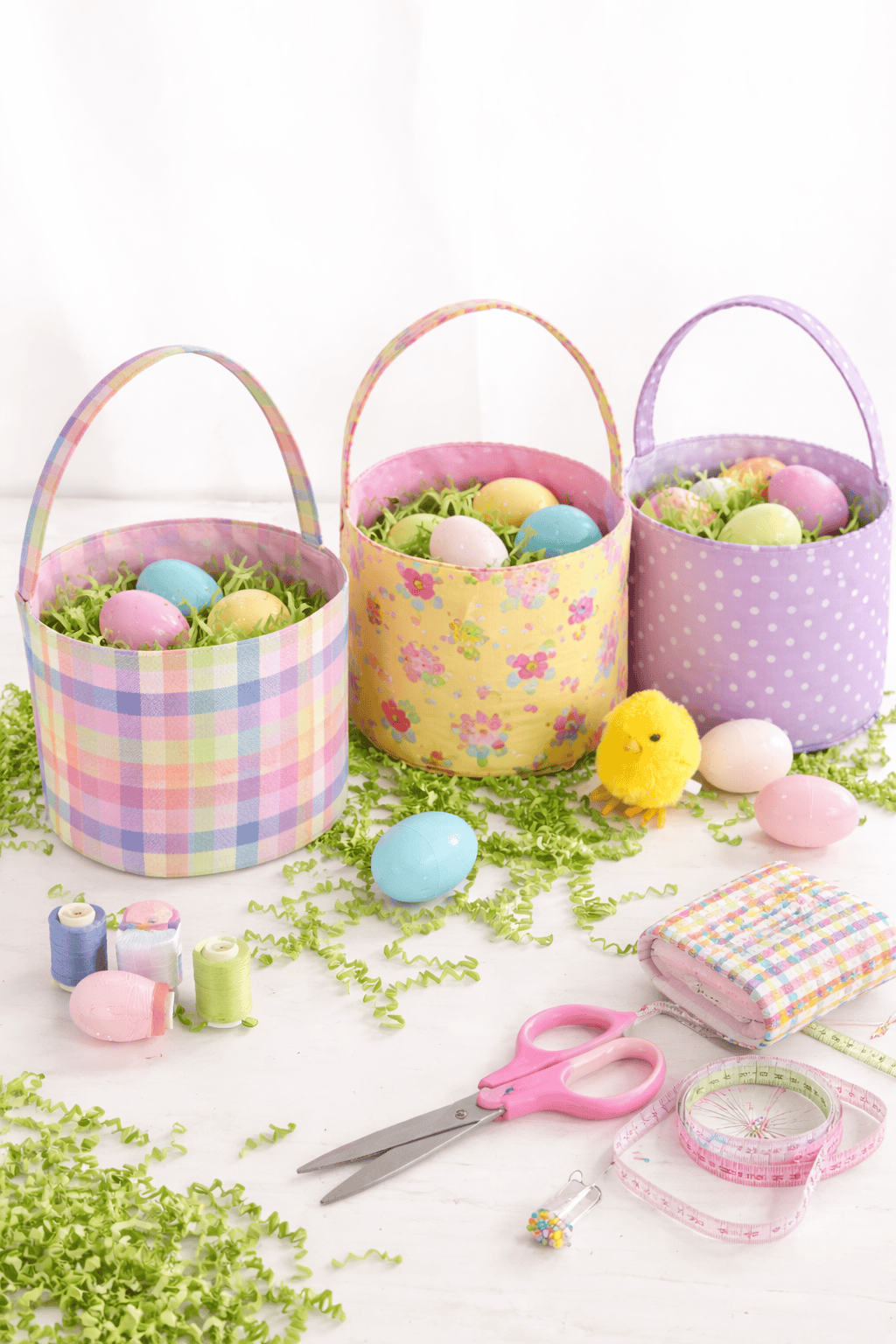 three pastel-colored Easter baskets arranged on a white wooden surface