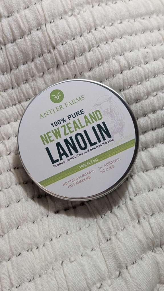 a round tin of “Antler Farms 100% Pure New Zealand Lanolin” placed on a soft, quilted fabric surface.
