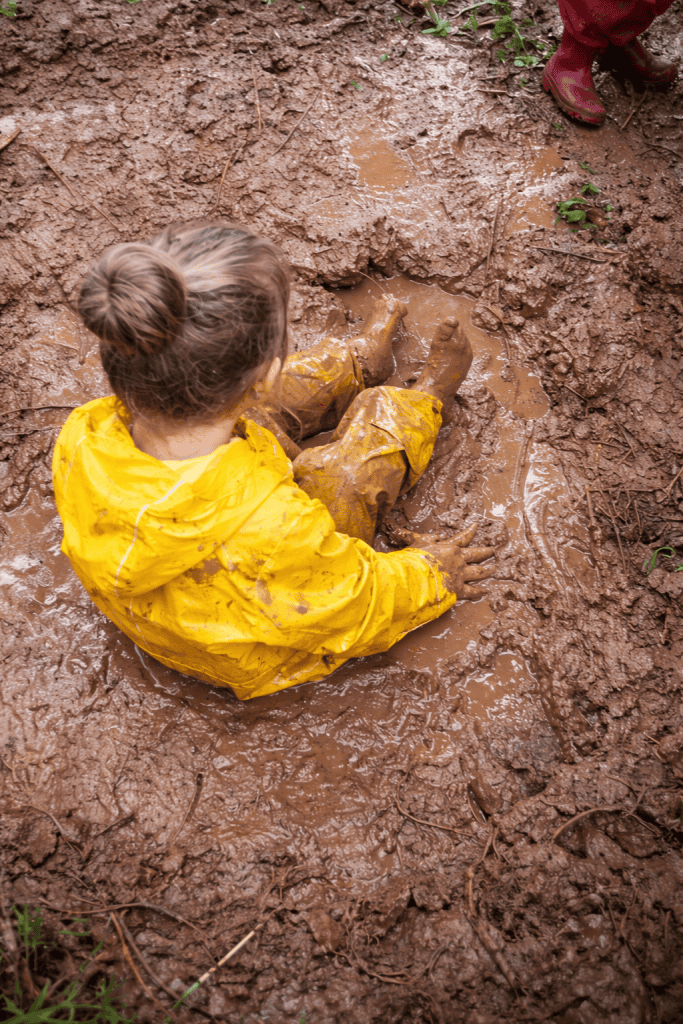 a young child joyfully sitting and playing in a muddy puddle on a forest floor.