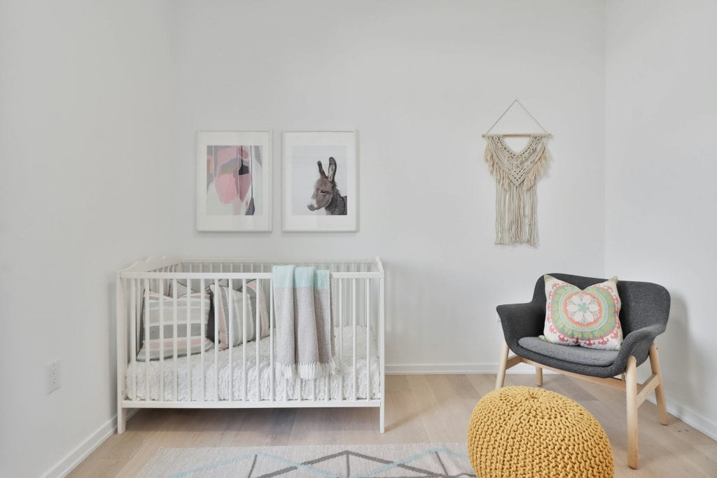 Minimalist nursery with white crib, organic cotton bedding, neutral wall art, and cozy chair in a light-filled baby room.