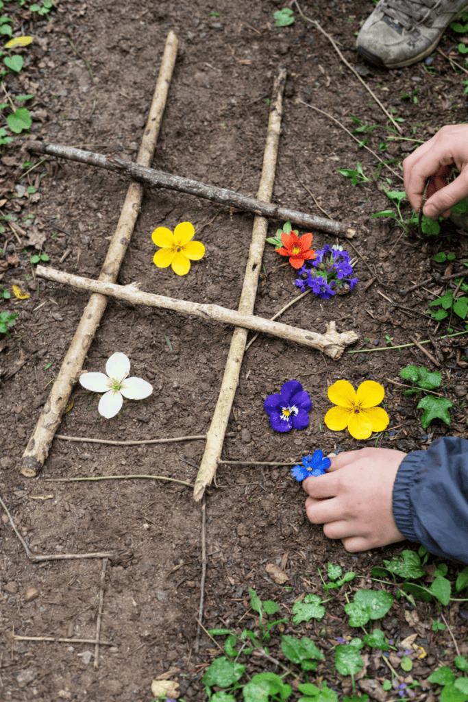 a children’s nature-based game of tic-tac-toe (noughts and crosses) made entirely from sticks and natural materials on a forest floor.