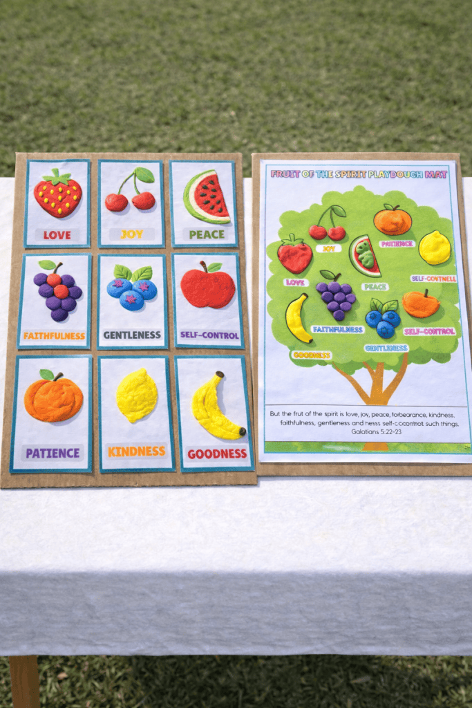 Fruit of the Spirit playdough crafts displayed side by side on a white outdoor table, showing fruit cards and a playdough tree mat activity for kids.