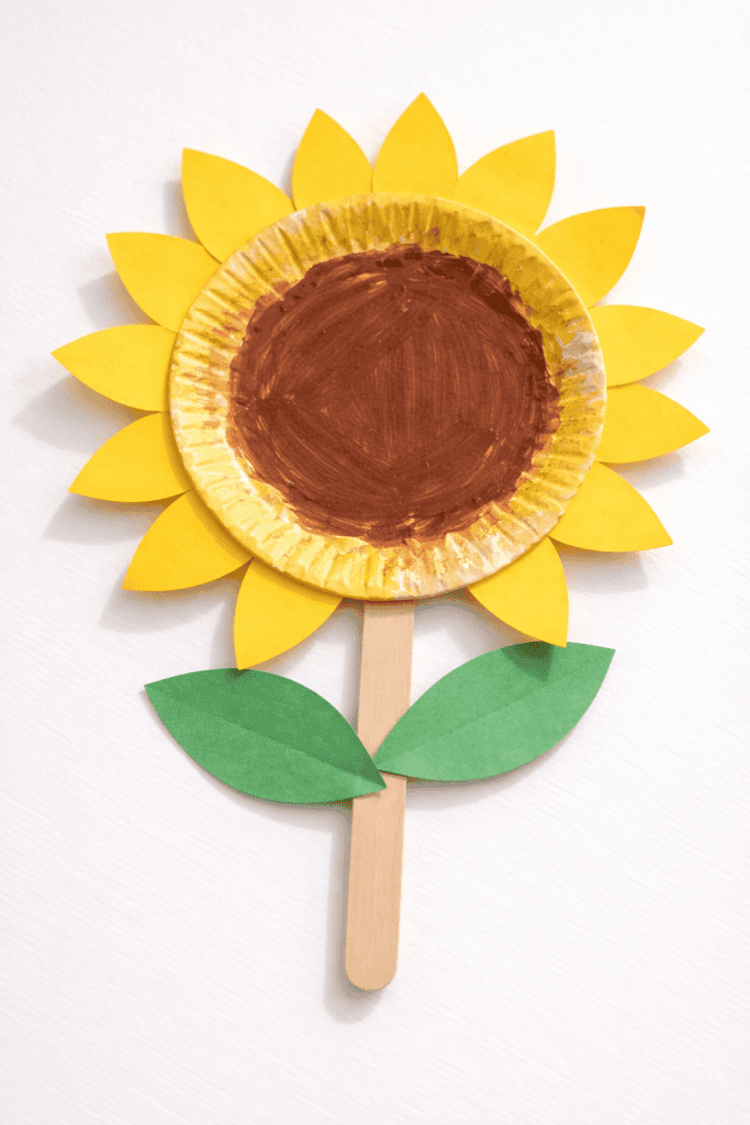 a kid-made sunflower paper plate craft placed on a plain bright white table