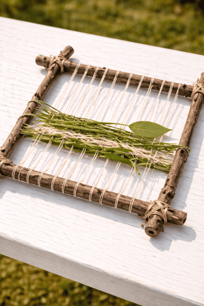 DIY nature weaving craft made with sticks, string, grass, and leaves for kids