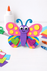 Colorful handmade butterfly craft with bright patterned wings and googly eyes on a clean white table.