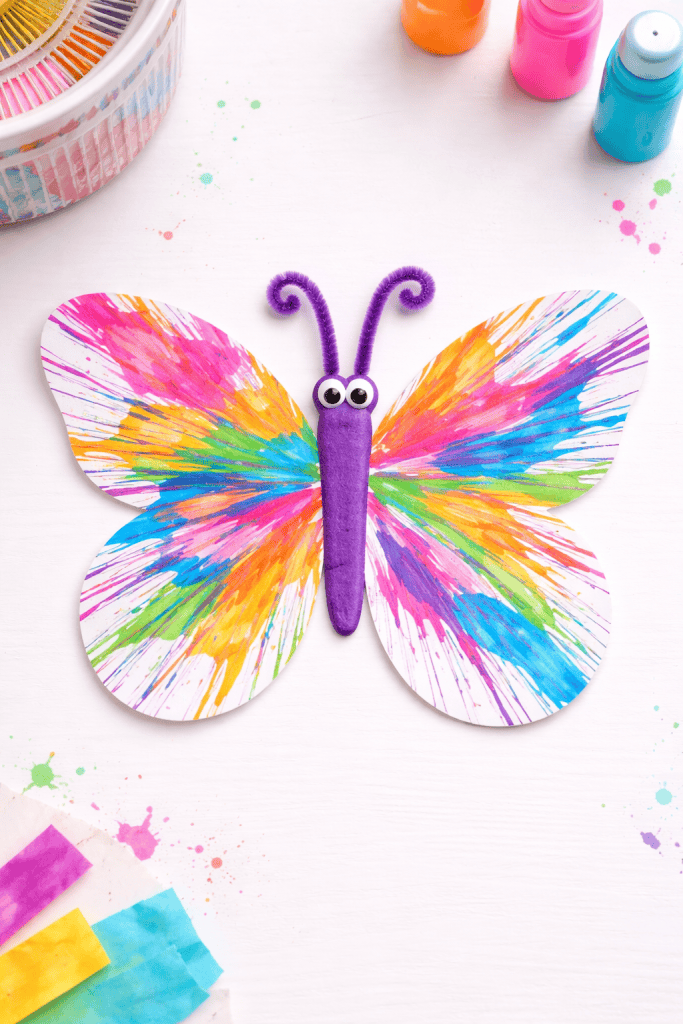 Colorful butterfly spin art painting on cardstock with streaky paint patterns on a white table.