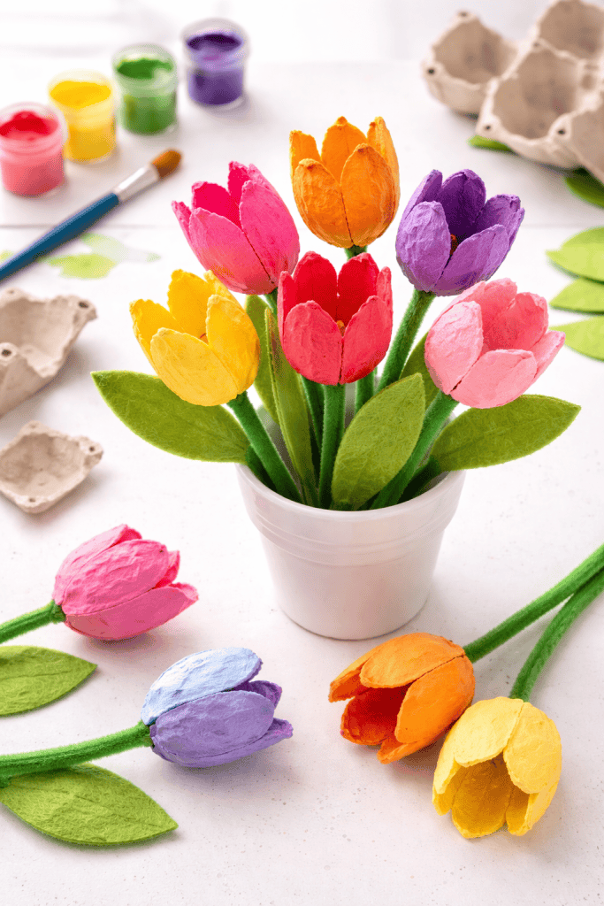 Colorful egg carton tulip crafts in a white pot with painted petals and green pipe cleaner stems