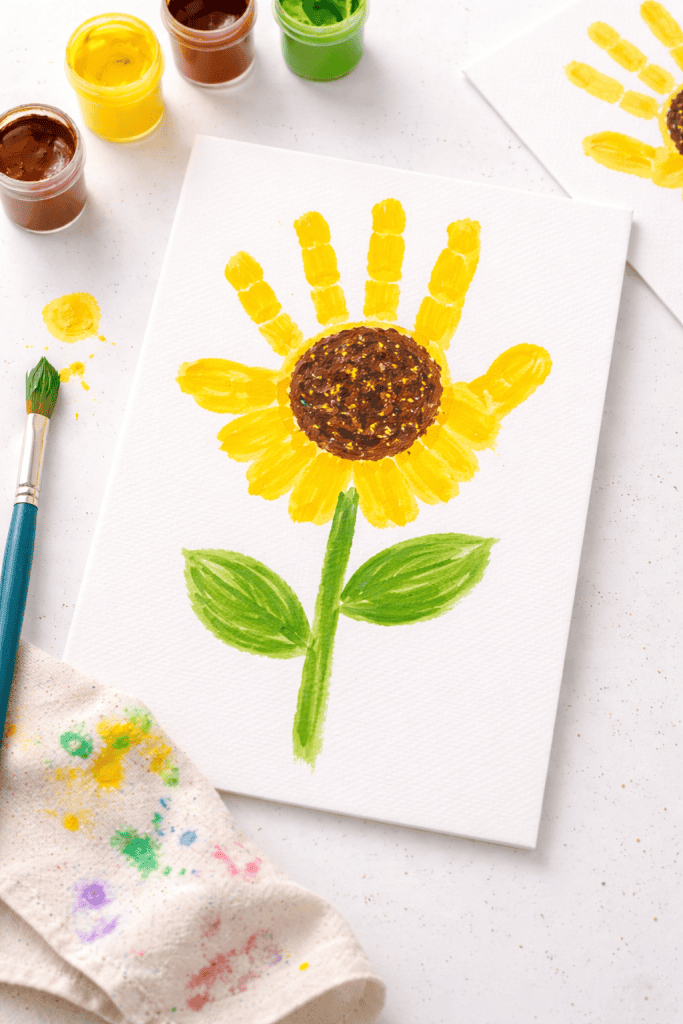 Kids’ handprint sunflower craft on white paper with bright yellow petals and green stem