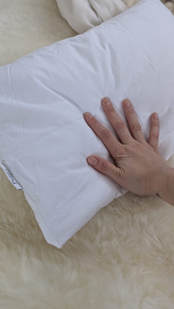 Hand pressing a soft white handmade pillow with wool filling to show its shape and firmness.