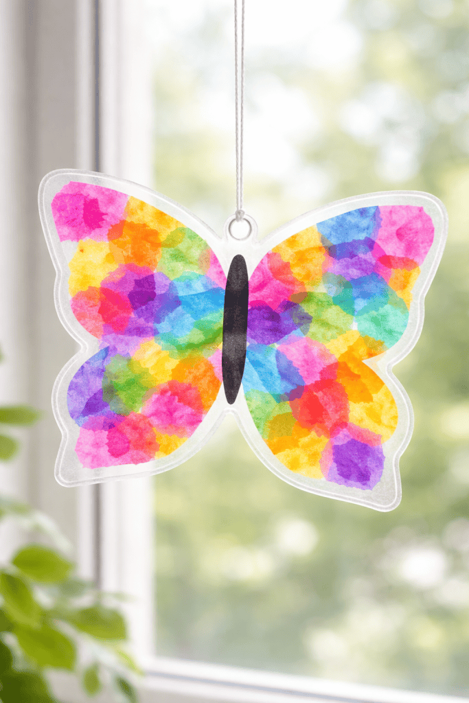 Colorful tissue paper butterfly sun catcher hanging in a bright window, glowing with sunlight.