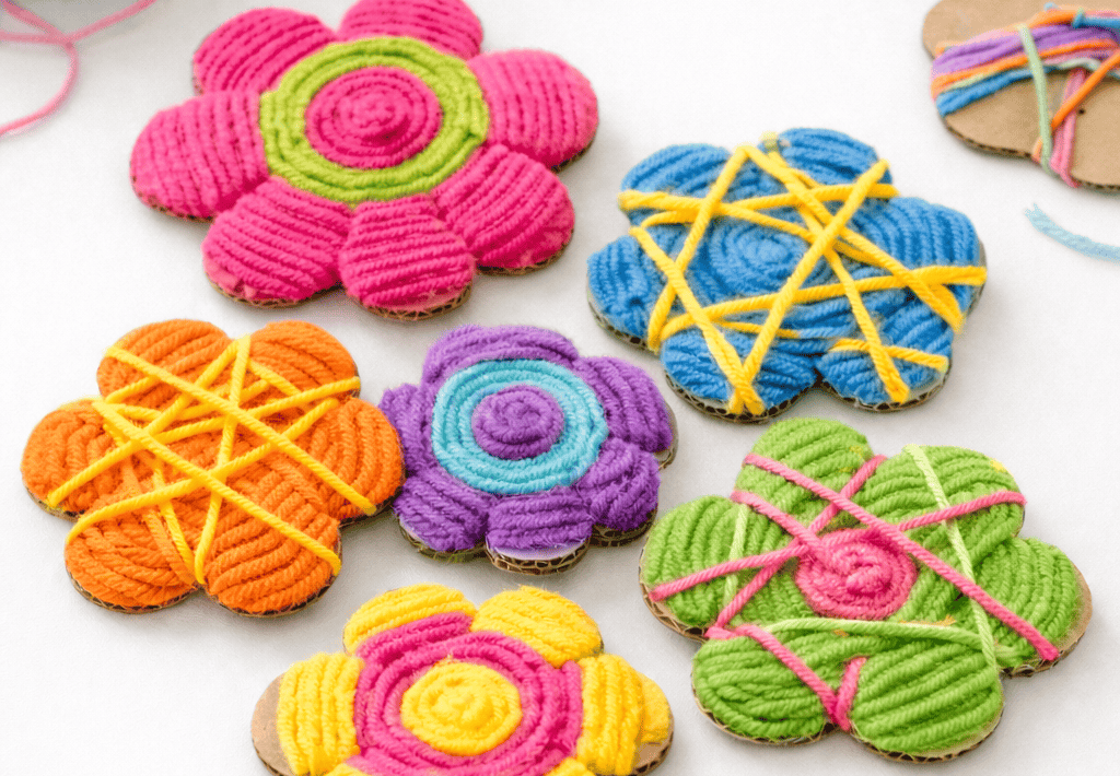 Colorful yarn-wrapped cardboard flowers fully covered in vibrant spiral and crisscross patterns, arranged on a clean white table