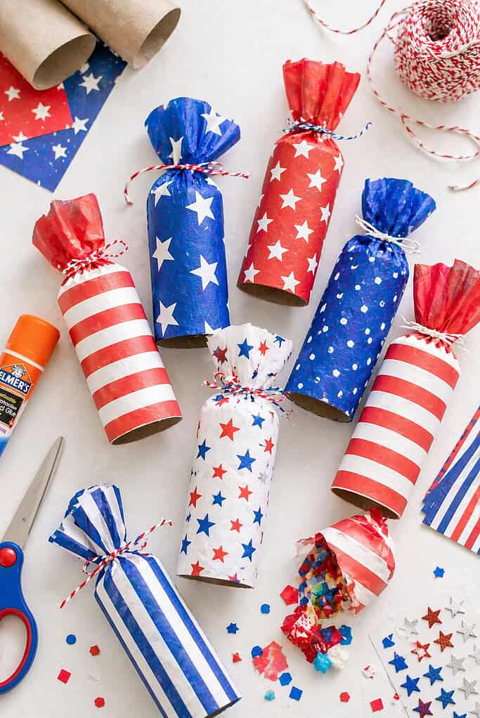Several toilet paper rolls transformed into festive “firecrackers,” wrapped neatly in red, white, and blue paper with a mix of patterns (stripes, stars, and solids)