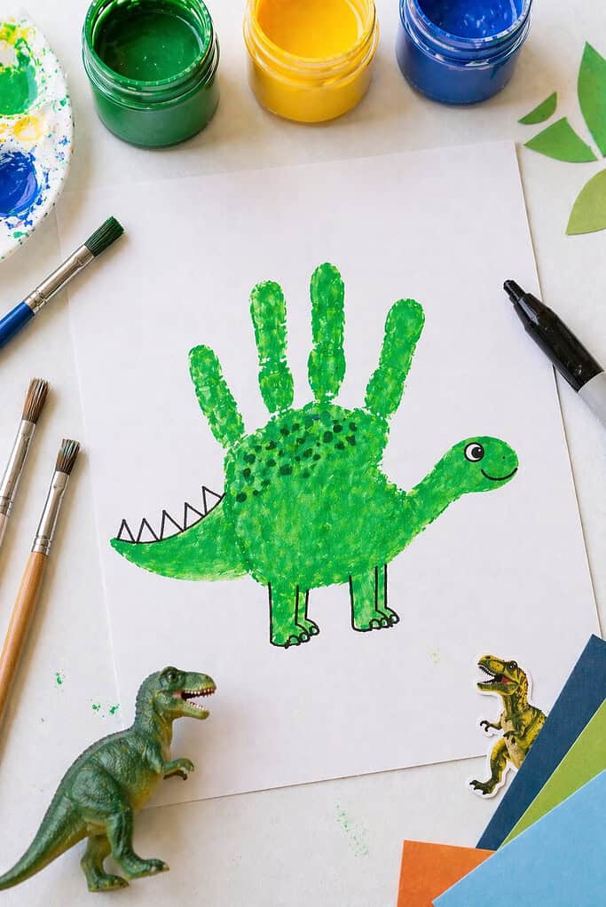 a finished dinosaur made from a sideways child’s handprint stamped in vibrant green paint