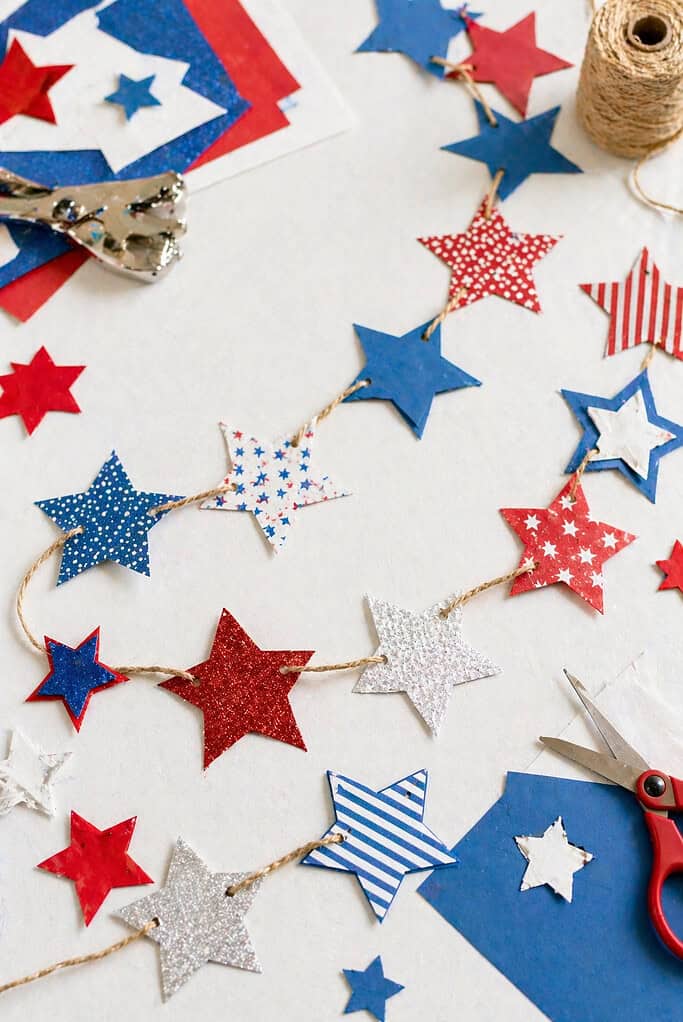 A handcrafted garland made of red, white, and blue stars cut from cardstock or lightweight cardboard.