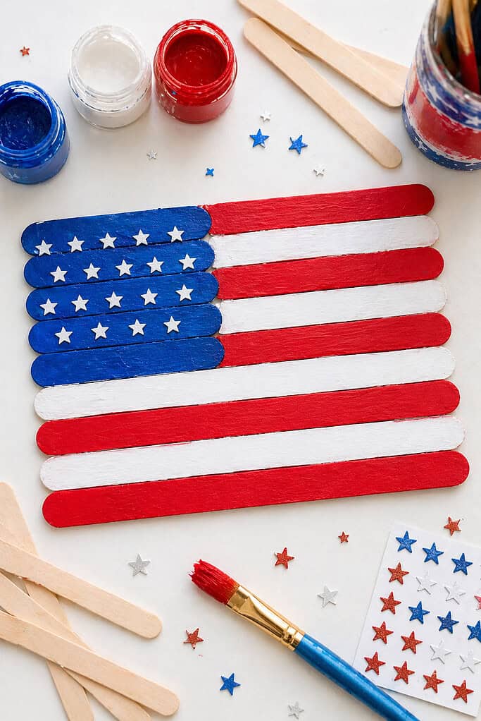 A handmade American flag constructed from aligned wooden popsicle sticks, placed horizontally and slightly centered.