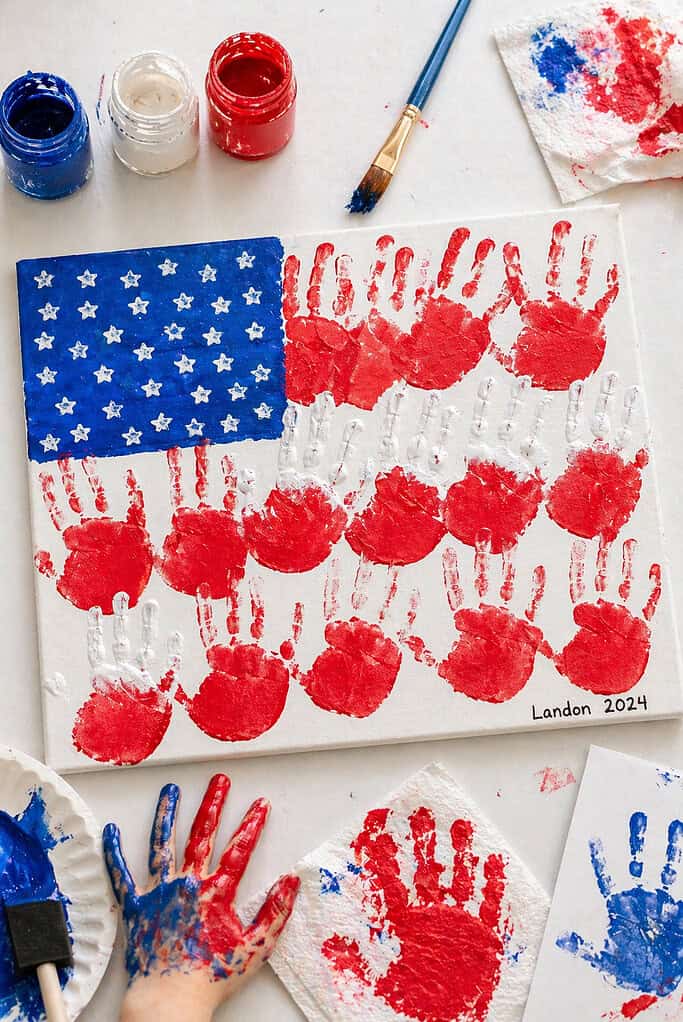 A piece of canvas or հաստ cardstock placed centrally, featuring overlapping child-sized handprints forming the American flag design