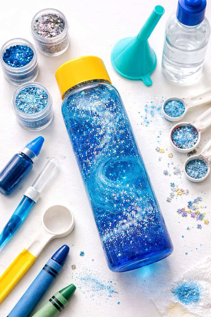 A clear plastic sensory bottle placed at the center, filled with water tinted in vibrant blue food coloring
