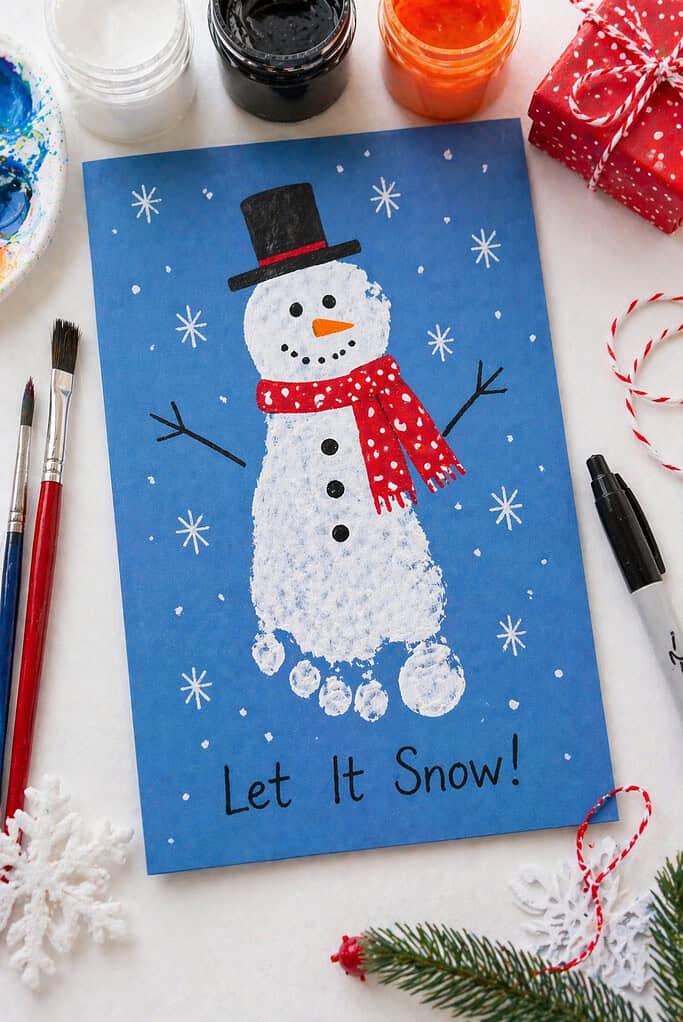 a finished holiday card featuring one or two white-painted child footprints forming a snowman.