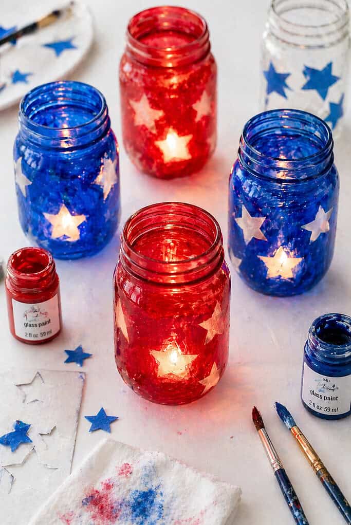 Several mason jars arranged in a loose cluster, each painted with translucent red and blue glass paint.