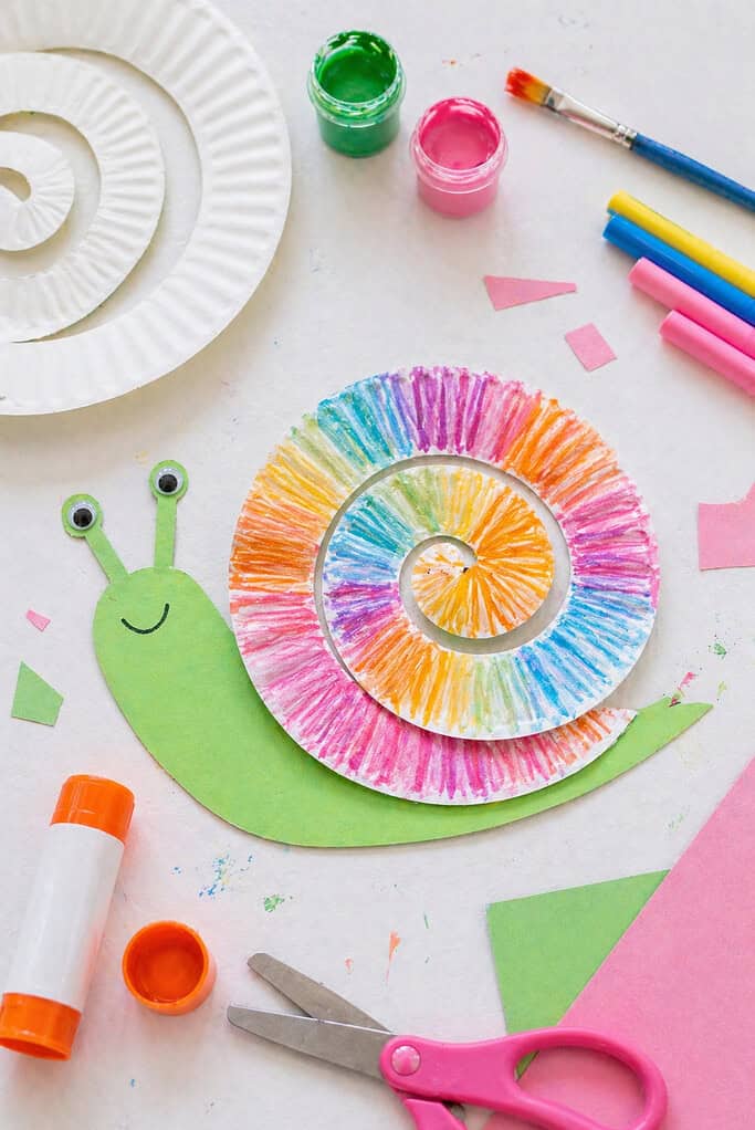 A paper plate cut into a spiral shape, forming the snail’s shell, decorated with colorful marker patterns or soft painted swirls