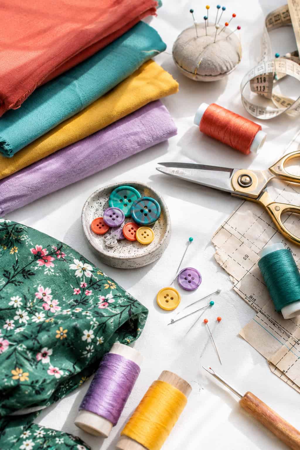 a stylish flat lay arrangement of colorful sewing materials and handmade clothing elements placed neatly on a bright white table