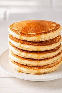 a stack of fluffy homemade pancakes on an elegant white ceramic plate