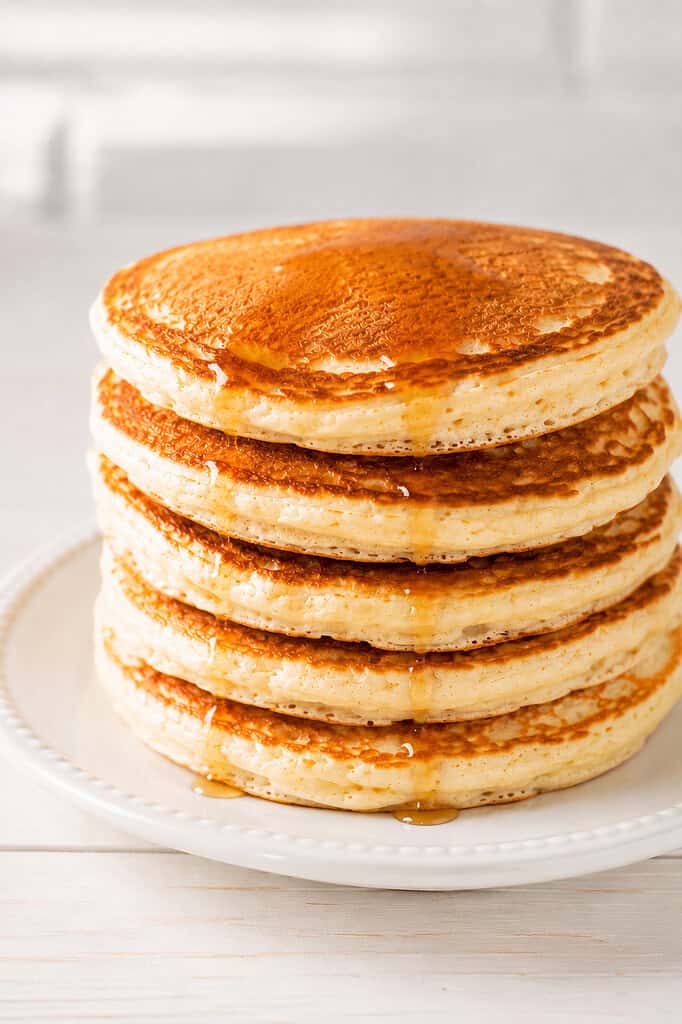 a stack of fluffy homemade pancakes on an elegant white ceramic plate