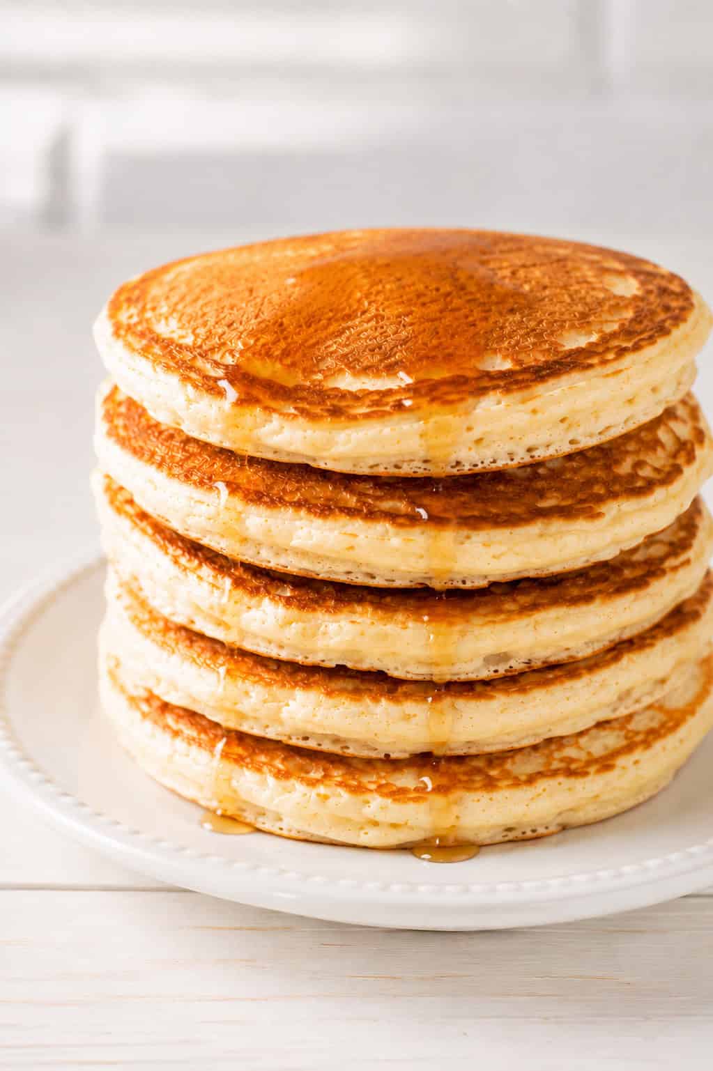 a stack of fluffy homemade pancakes on an elegant white ceramic plate